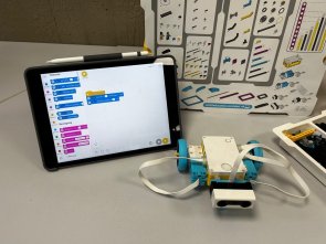 Auf einem Tisch stehen die Utensilien für Lego-Spike: Tablet, Plan mit den einzelen Legobausteinen, Legobausteine und das Anfangsmodell für den Roboter.