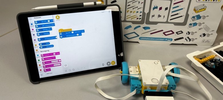 Auf einem Tisch stehen die Utensilien für Lego-Spike: Tablet, Plan mit den einzelen Legobausteinen, Legobausteine und das Anfangsmodell für den Roboter.