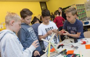 4 Schüler stehen an einem Tisch. Sie basteln an einem Windrat, das auf dem Tisch steht.
